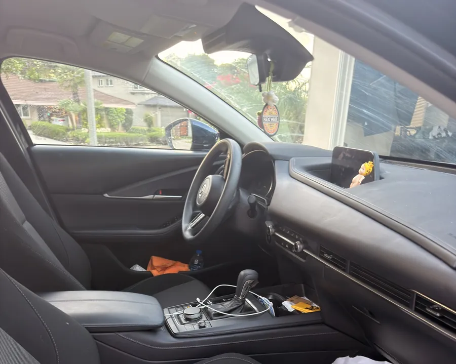 The front cabin of a Mazda3 before detailing: papers on the seat, clutter across the centre console and dust on the dash