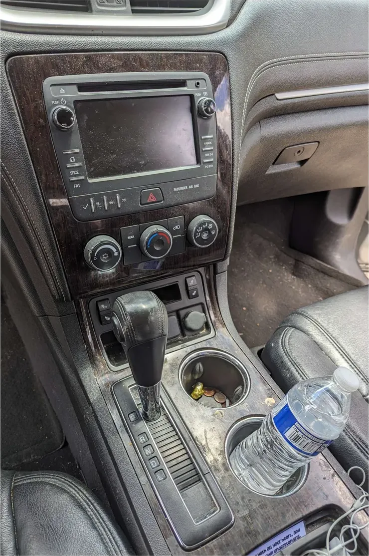 The center console and dash of an SUV before detailing: sticky wood trim, coins in a cupholder, smudged screen