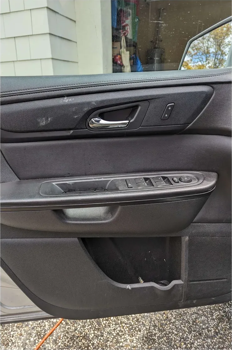 A front door panel before detailing: scuffs and smudges on the armrest and handle area, debris in the door pocket