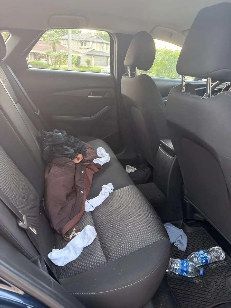 The back seat of a Mazda3 before detailing: a jacket, loose socks and empty water bottles across the bench and the floor