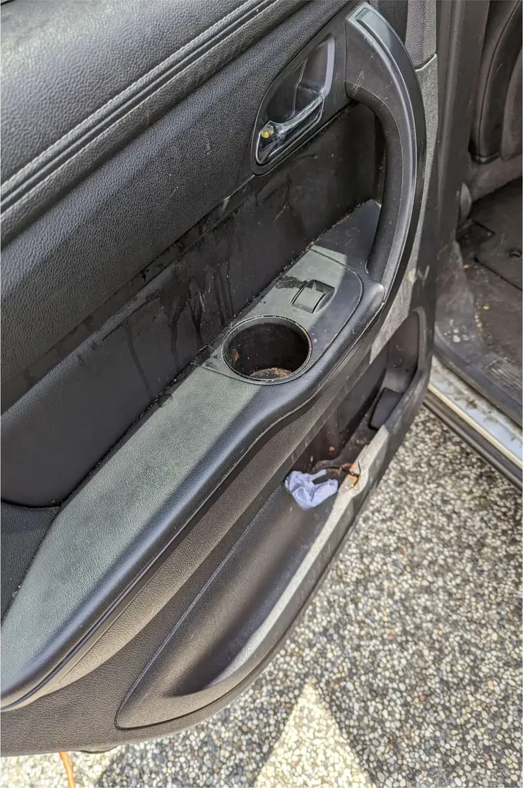 A rear door panel before detailing: drip stains running down the panel, grime in the cupholder, trash in the pocket