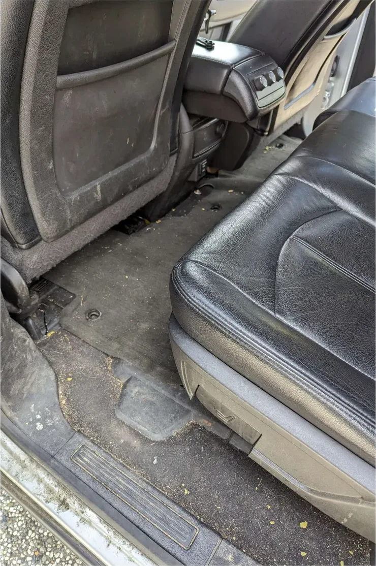 The rear footwell of an SUV before detailing: dirt and leaves ground into the carpet, scuffed seat back
