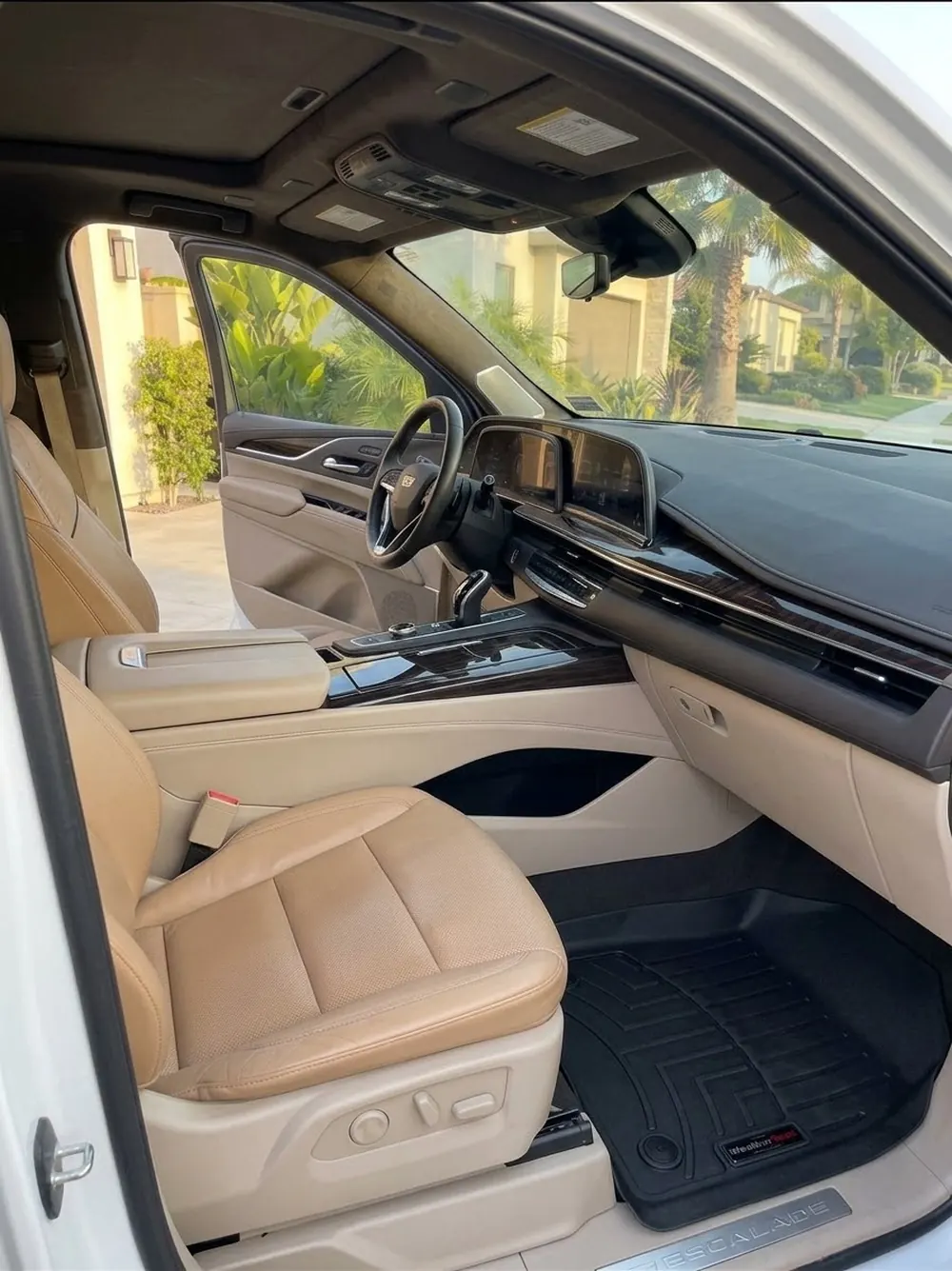 The front cabin of a Cadillac Escalade after an interior detail: tan leather seats, wood and piano-black trim wiped down, floor liners cleaned