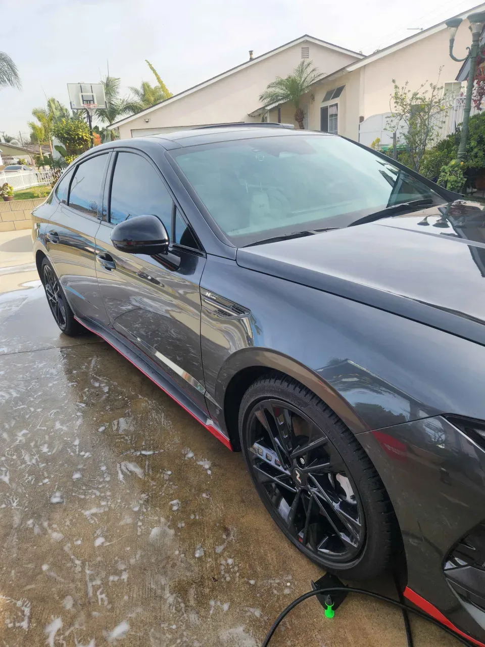 A dark gray Hyundai sedan with red trim just after a hand wash, paint glossy and wheels clean, parked in a residential driveway
