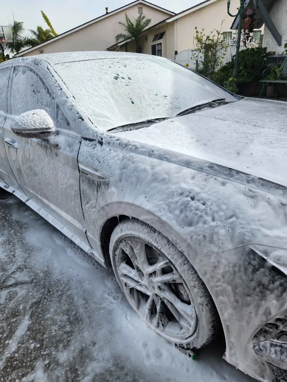 The same Hyundai covered in thick white foam from roof to wheels during the foam pre-wash