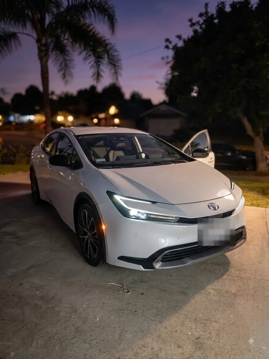 A white Toyota Prius washed and waxed, parked on a driveway at dusk with the paint reflecting the sky