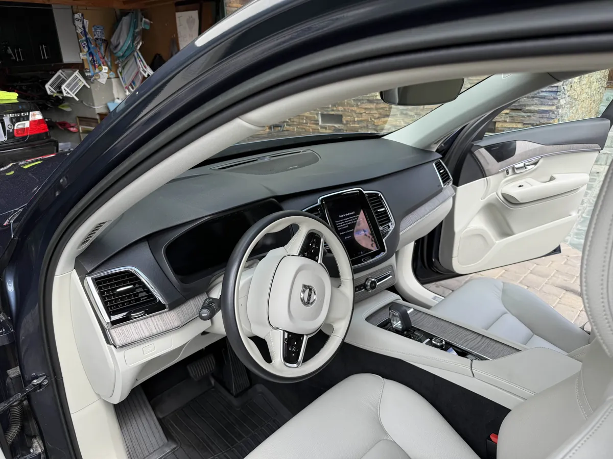 The front cabin of a Volvo SUV with light cream leather seats, white steering wheel and light wood trim after an interior detail