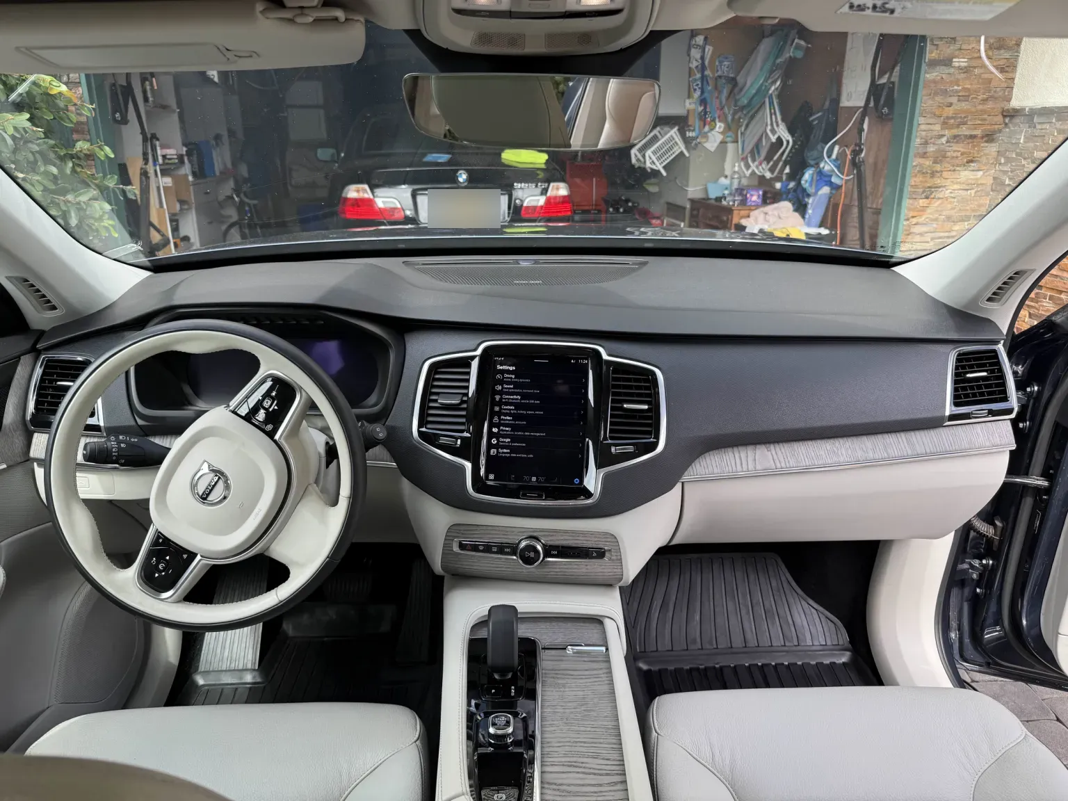 Straight-on view of a Volvo dashboard after detailing: cream leather, center screen, wood console and rubber floor liners cleaned